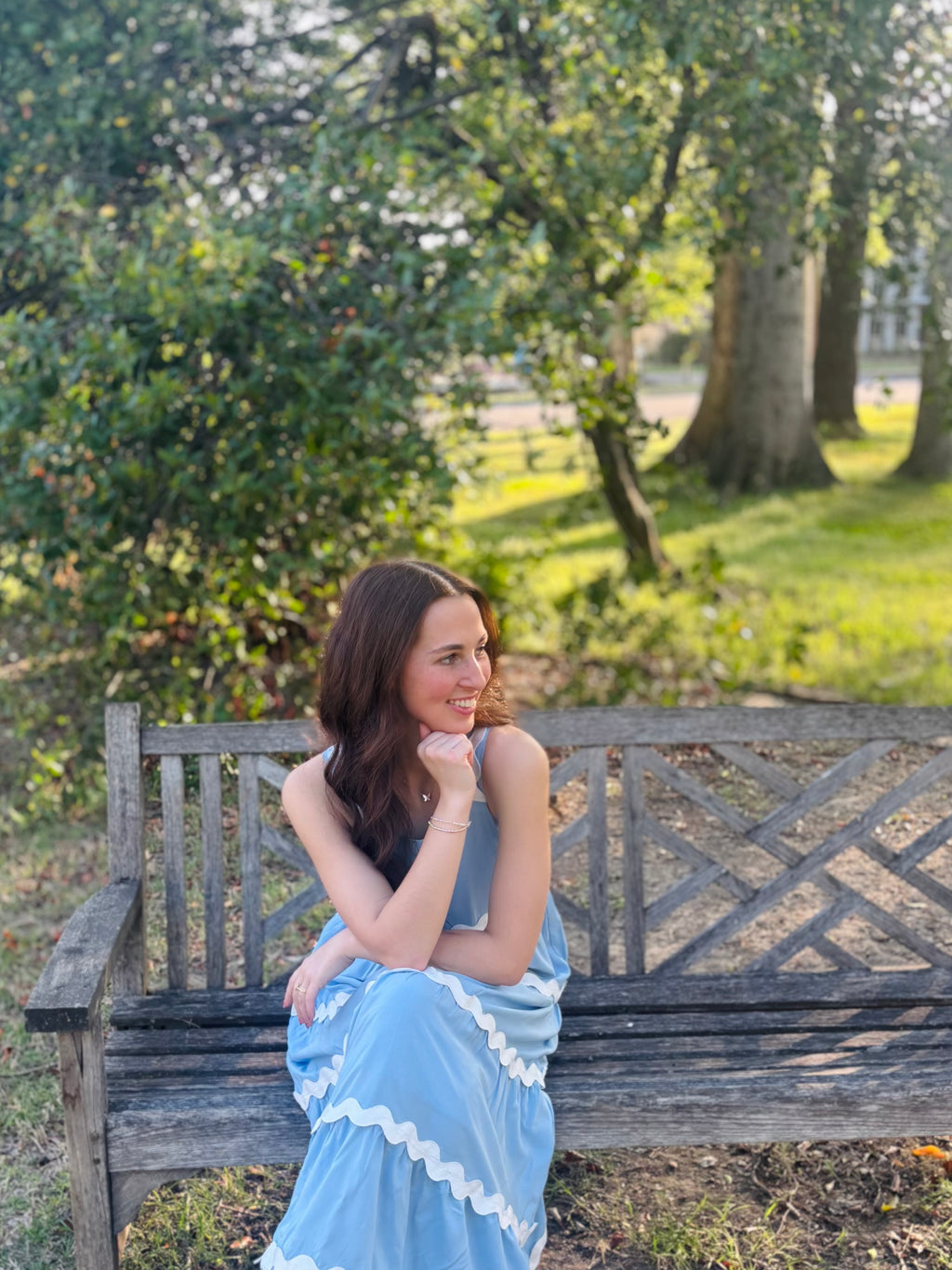 Woman in a blue dress sitting on a wooden bench in a park.
