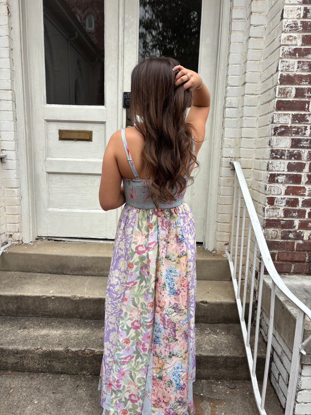 Person wearing a floral dress standing in front of a building with a brick facade.