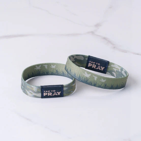 Two wrist bands with 'TAP to Pray' text and earthy tones and doves in the background of the wristband on a white background showing the two reversible sides to it