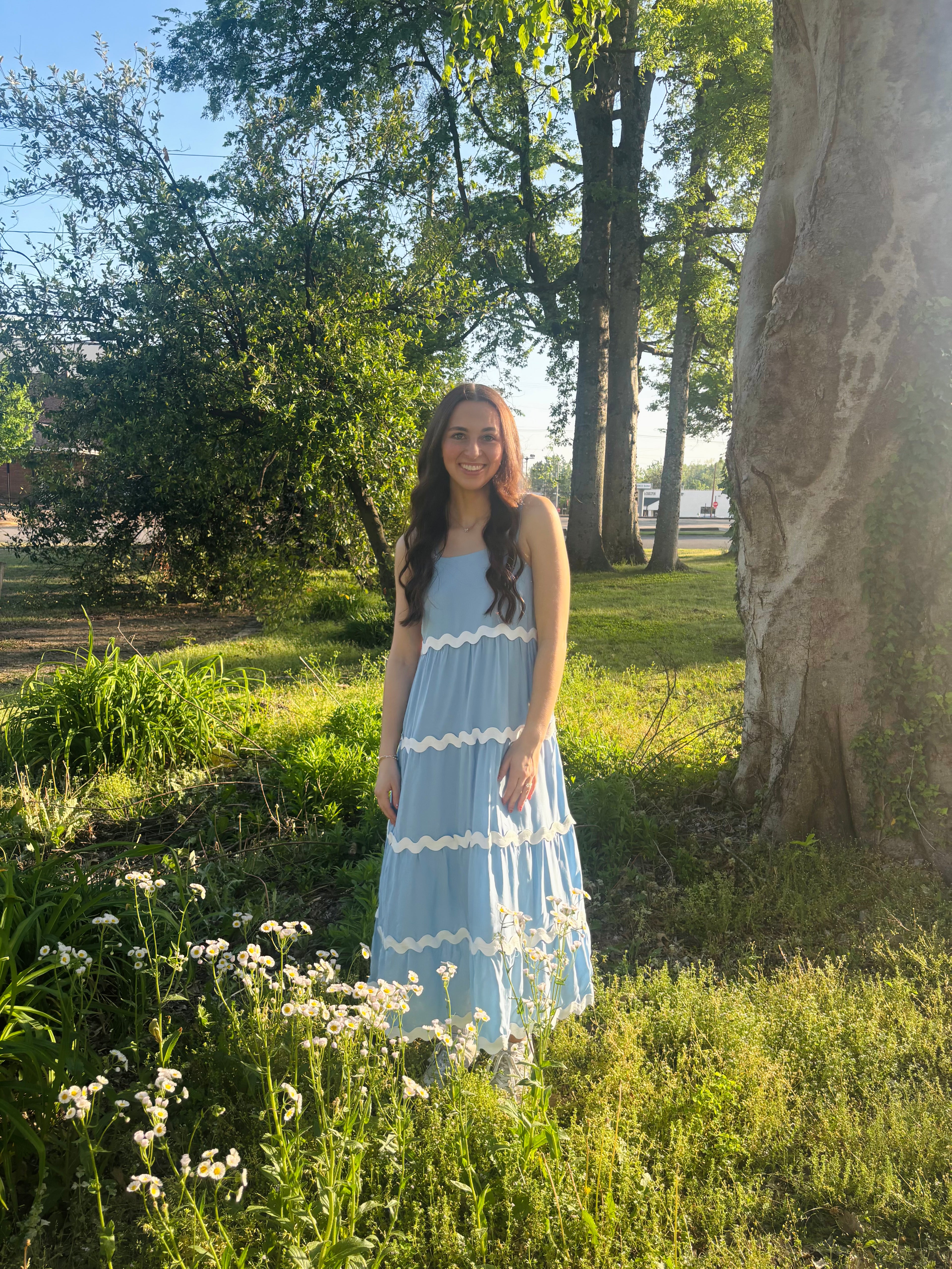 Woman in a light blue dress standing in a grassy field with trees in the background