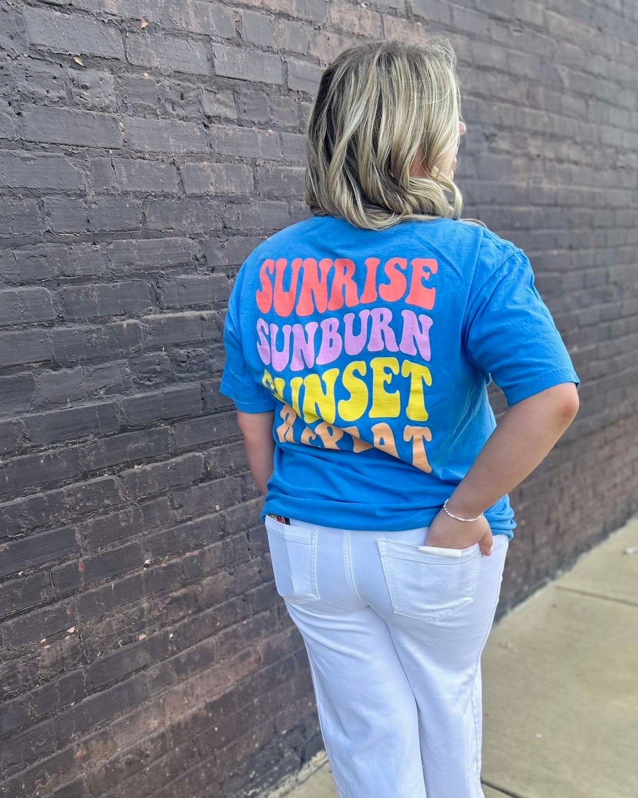 Person wearing a blue t-shirt with colorful text against a brick wall.