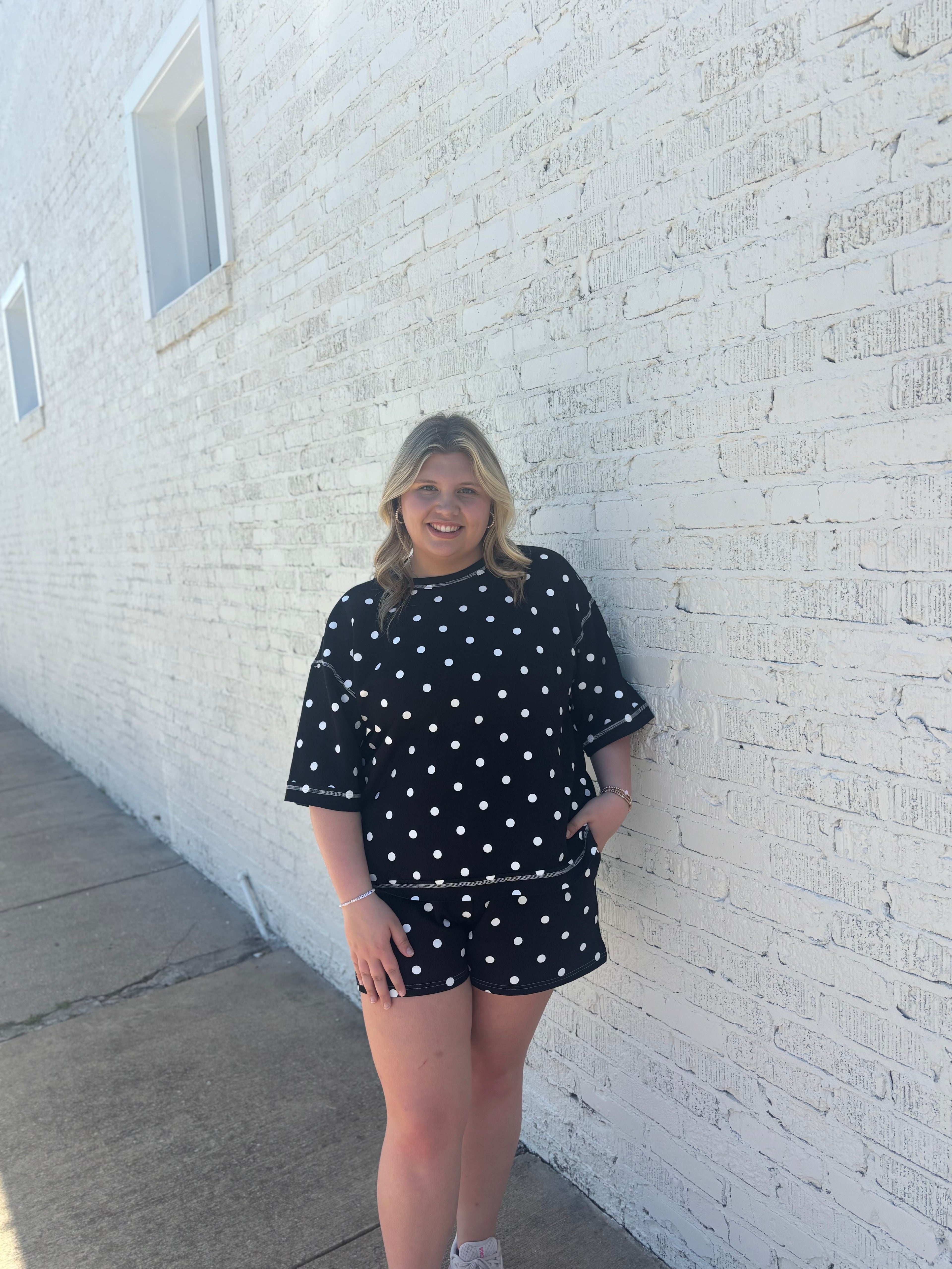 Girl wearing a black and white polka dot set standing against a white brick wall