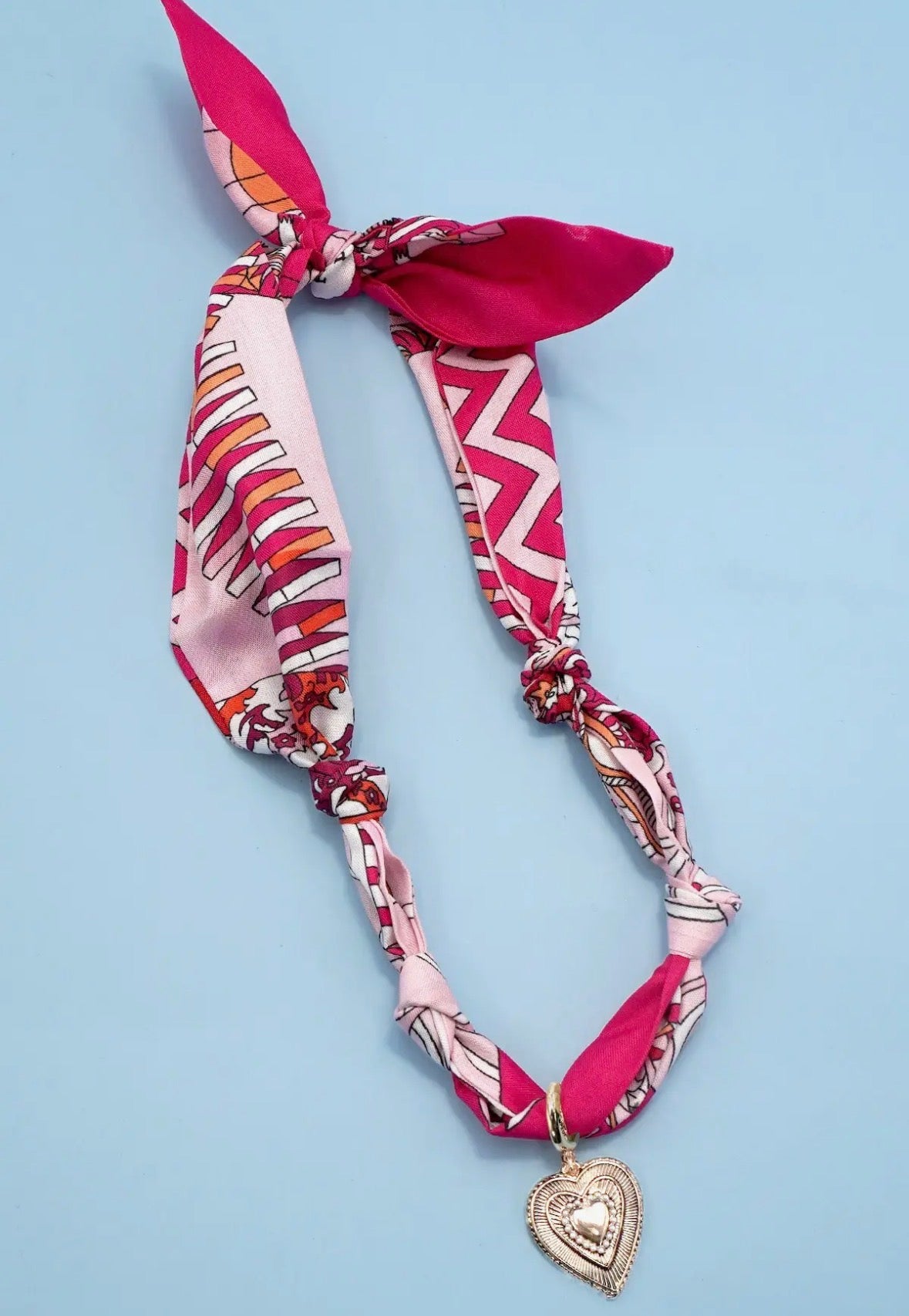Decorative headband with pink and white pattern and heart charm on a light blue background