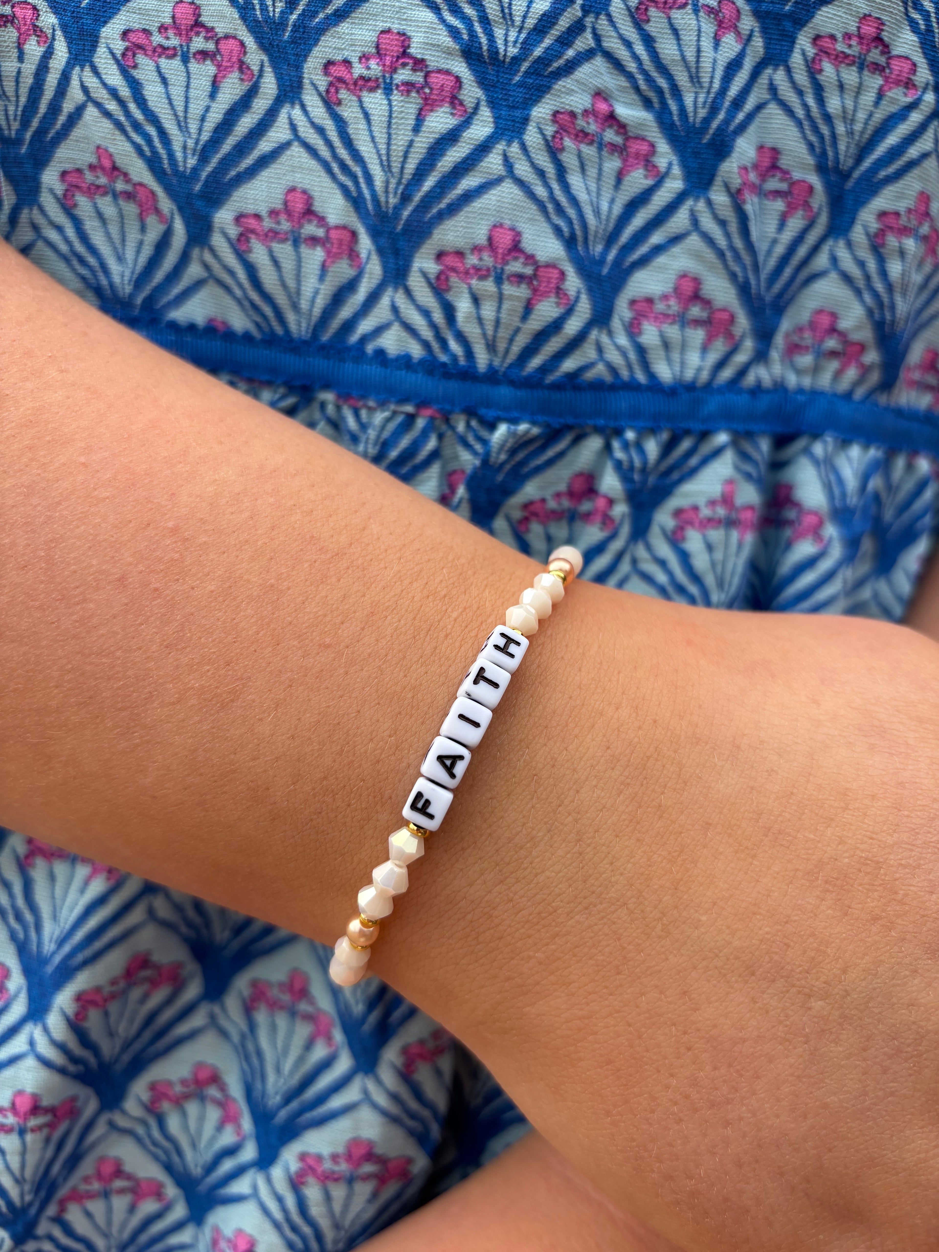 Bracelet with letter beads on a wrist against a blue and pink patterned fabric background