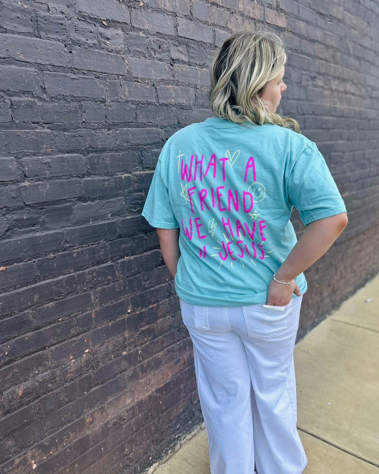 Person wearing a light blue t-shirt with text against a brick wall.