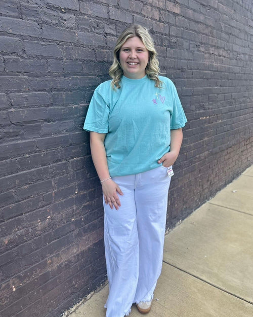 Person wearing a light blue t-shirt and white pants standing against a brick wall.