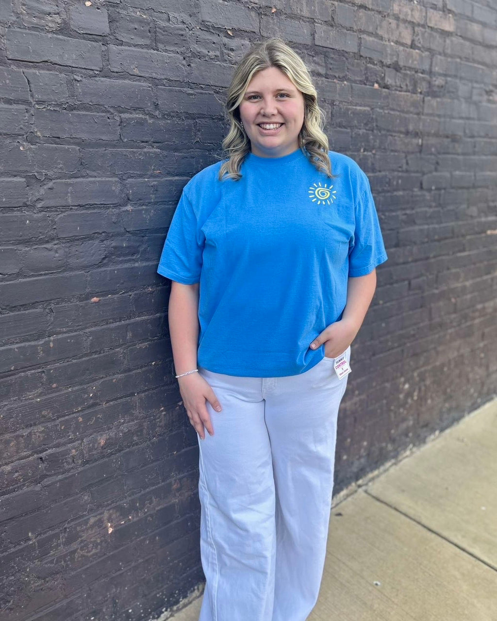 Person wearing a blue t-shirt with a logo against a brick wall.
