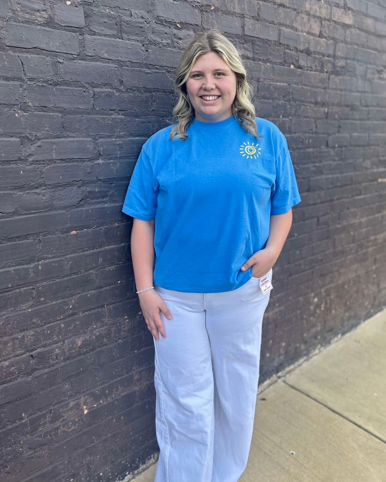 Person wearing a blue t-shirt with a logo against a brick wall.