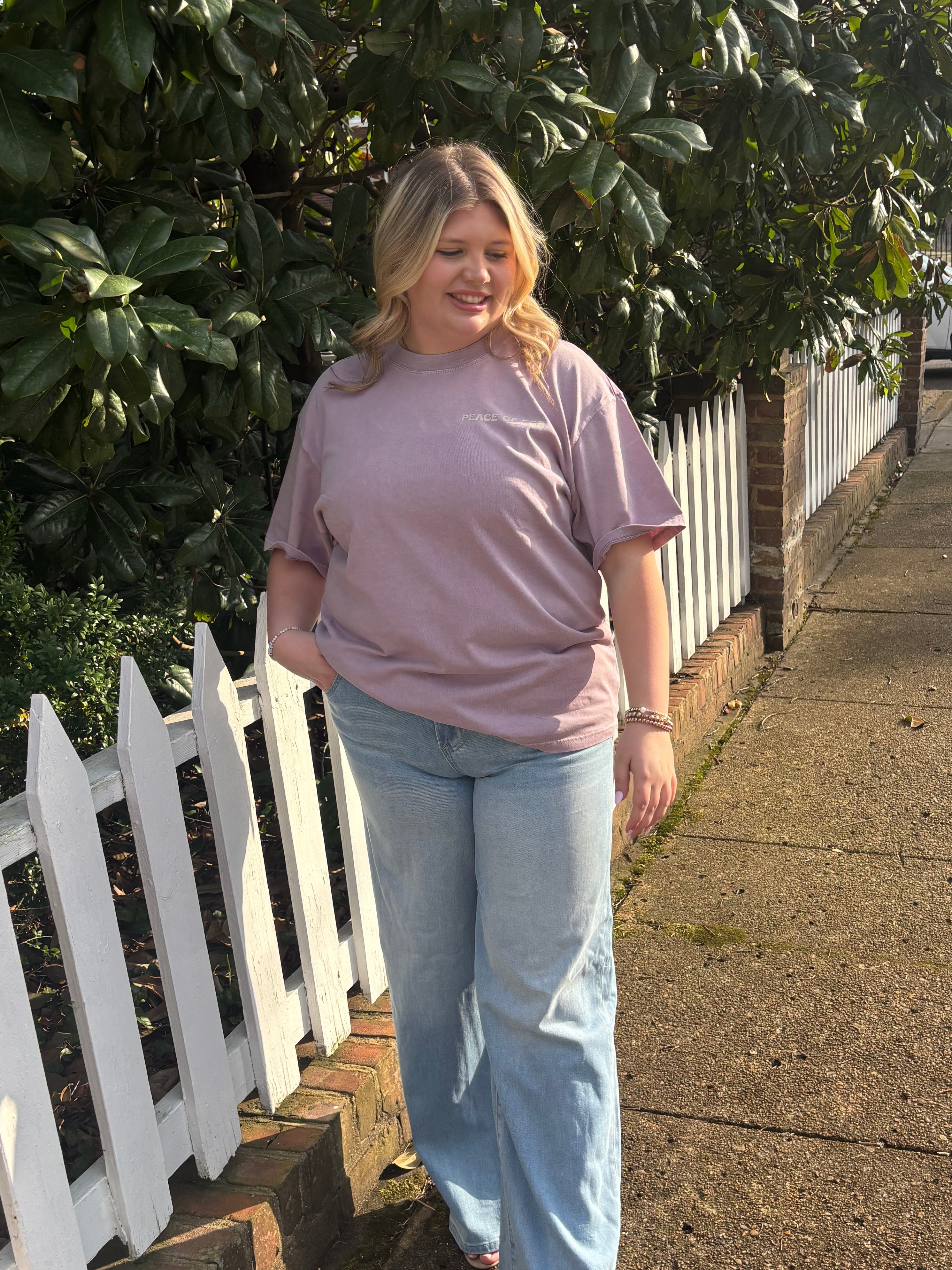 Woman standing on a sidewalk next to a white picket fence with greenery in the background