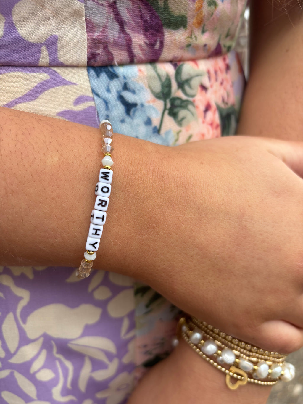Bracelet with 'WORTHY' beads on a wrist against a floral fabric background