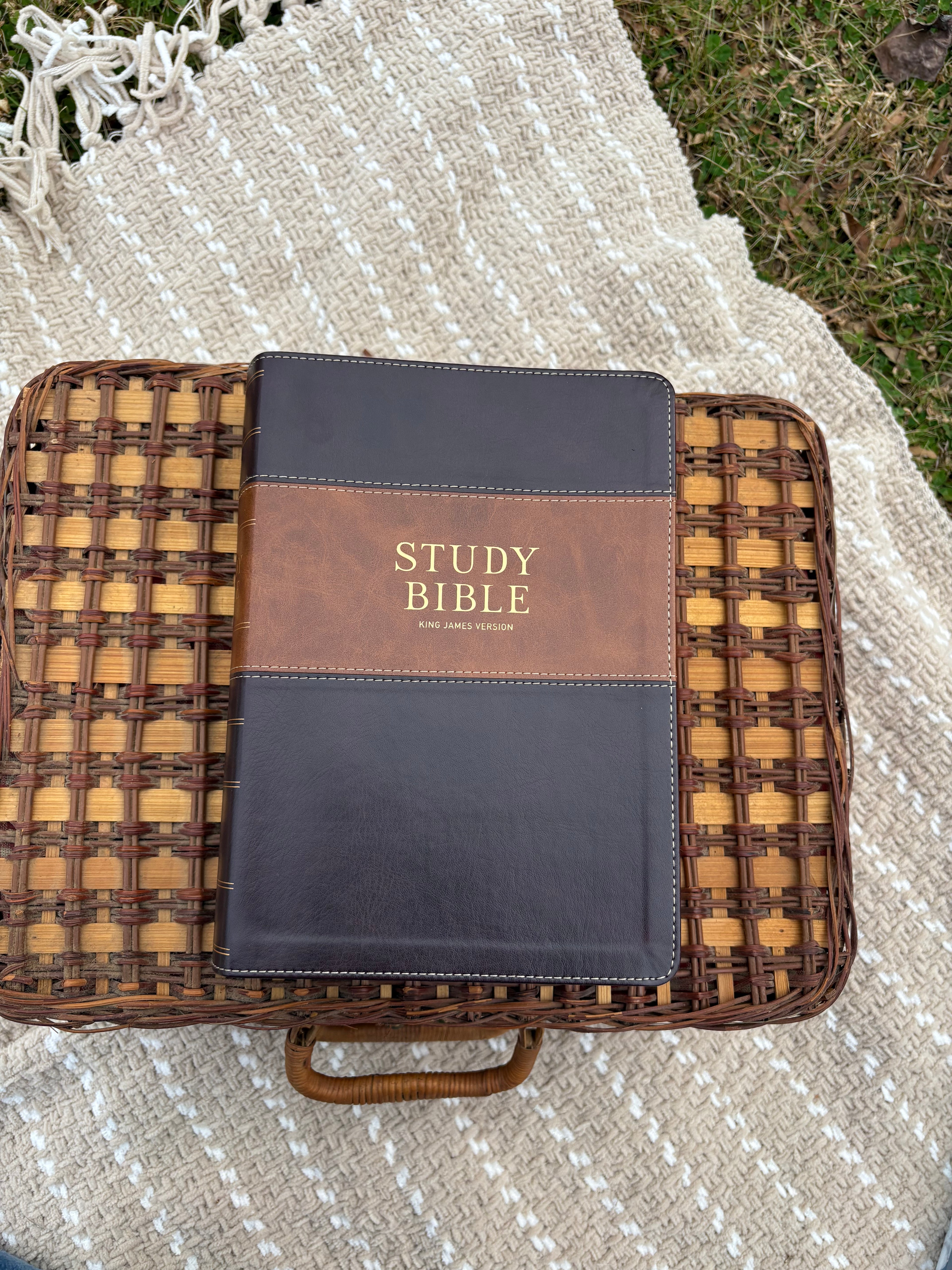 Burgundy study bible laying on wicker basket on a beige blanket in the outdoors