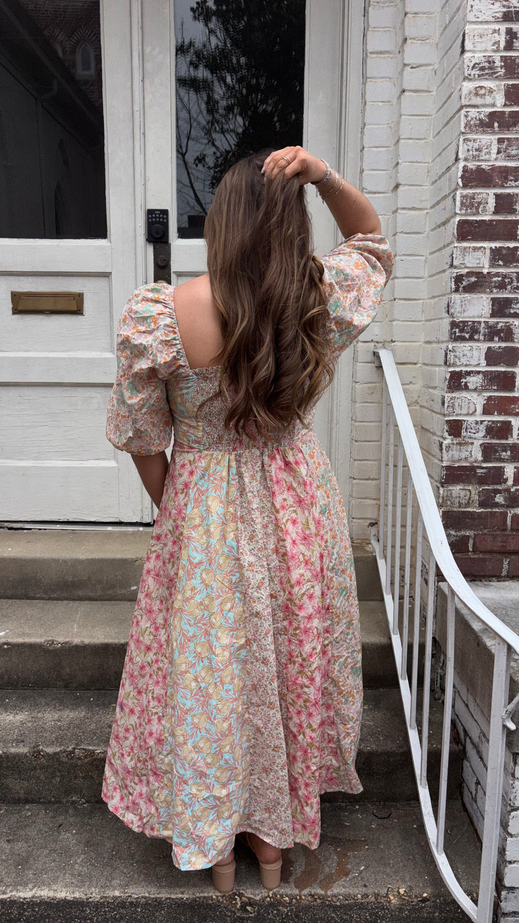 Woman in a floral dress standing on steps outside a house.