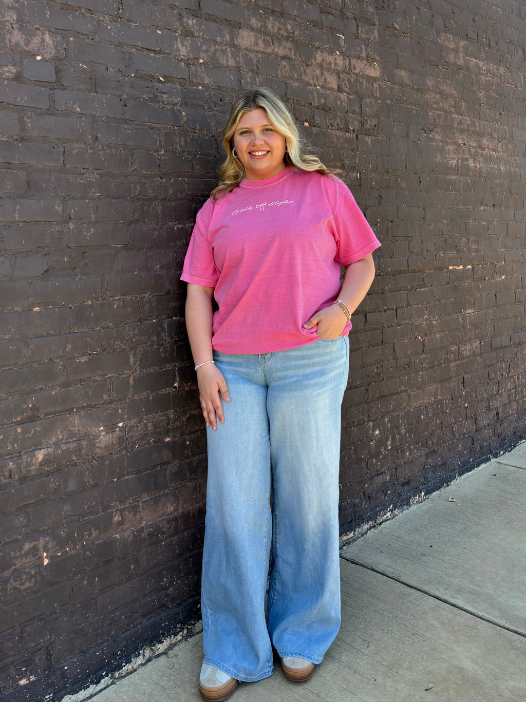 Girl wearing a pink shirt with denim jeans standing infront of a black brick wall
