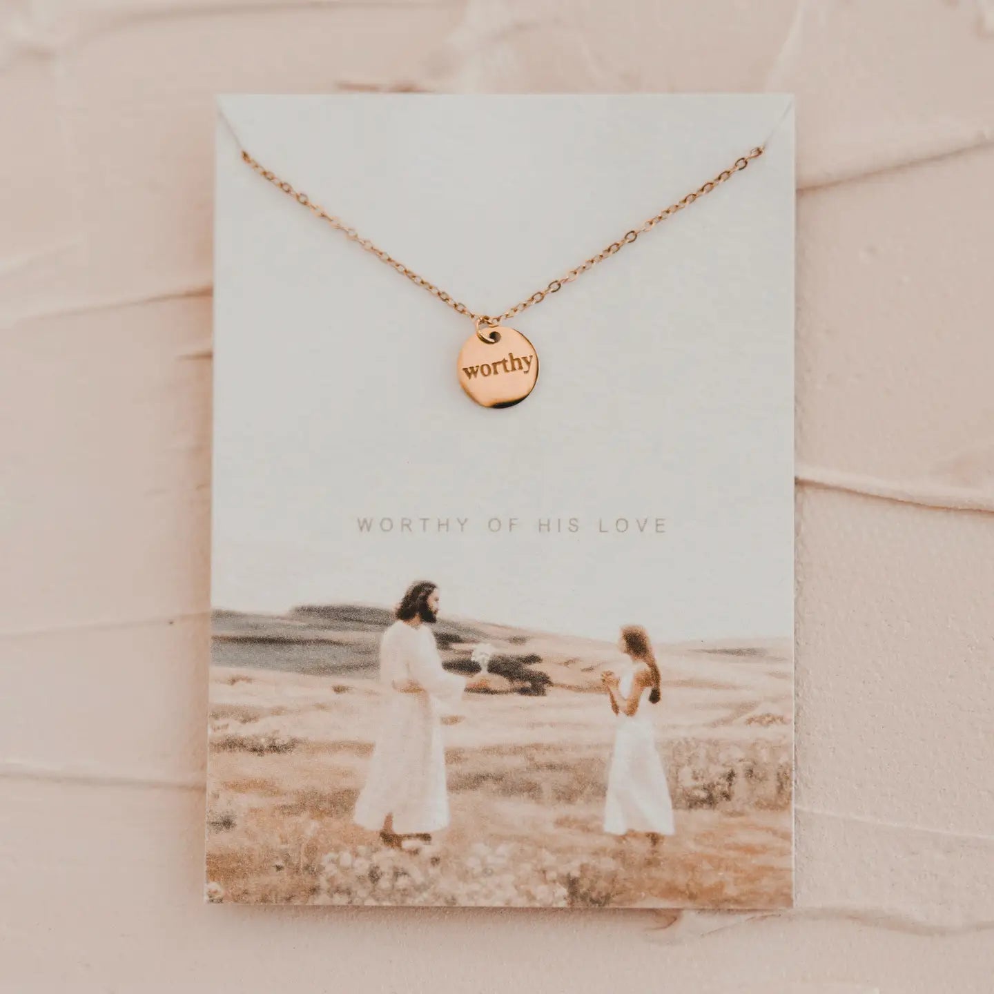 Rose gold necklace with 'worthy' pendant on a card with a photo of a woman and child in a field.