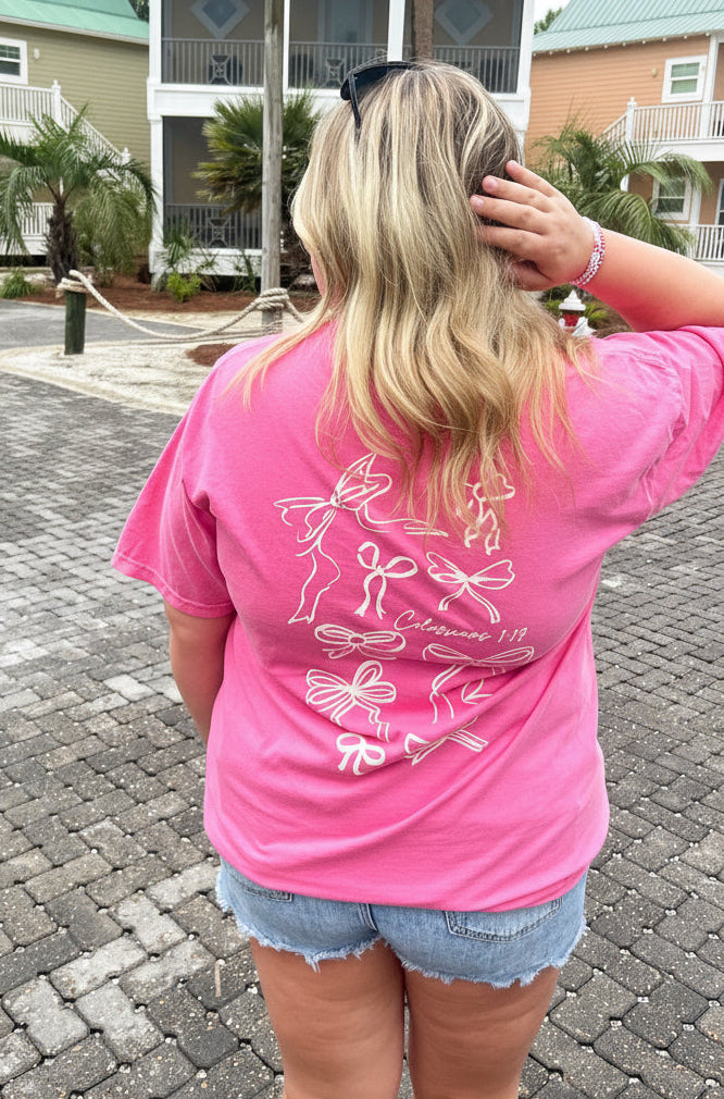 Person wearing a pink t-shirt with a design on the back, standing on a brick driveway with houses in the background.