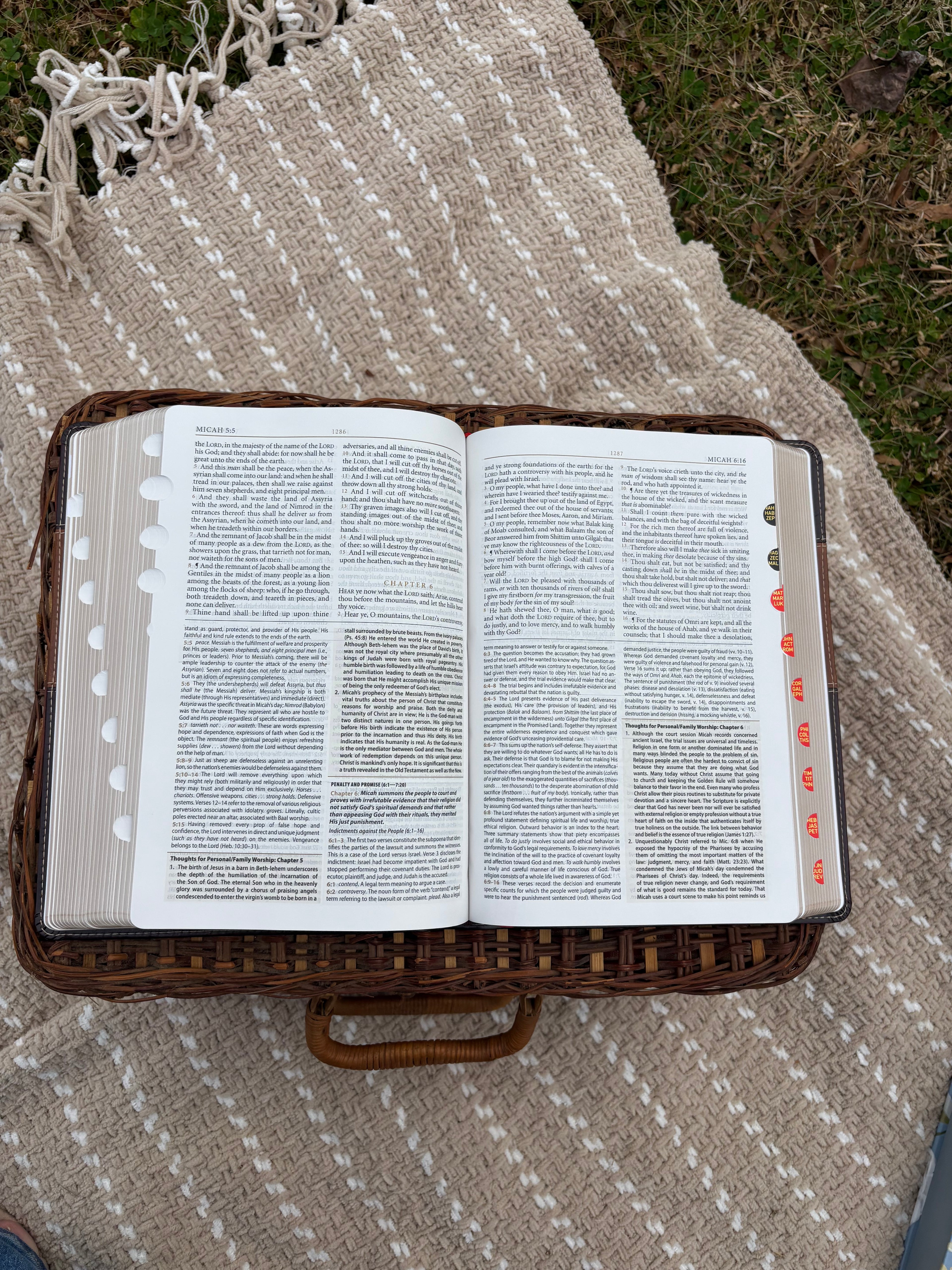 Open Bible laying on a wicker basket on a textured blanket outdoors