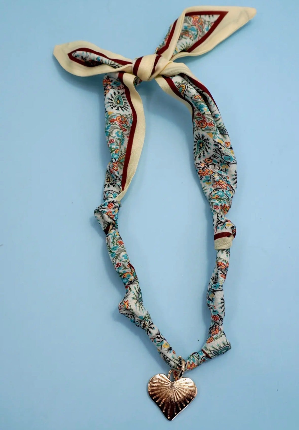 Decorative headband with floral pattern and heart-shaped pendant on a light blue background