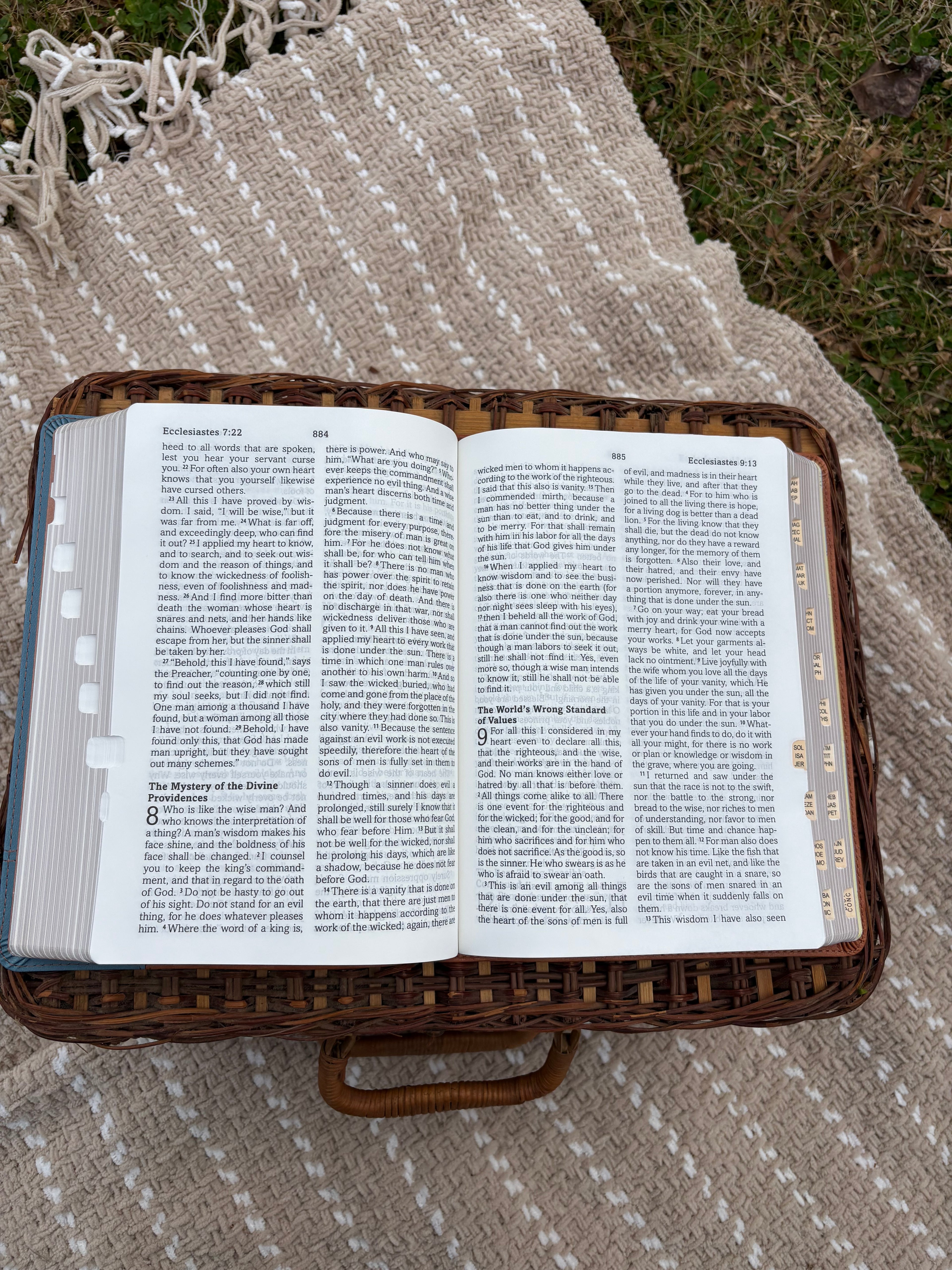 Open bible on a woven basket outdoors on a beige textured blanket