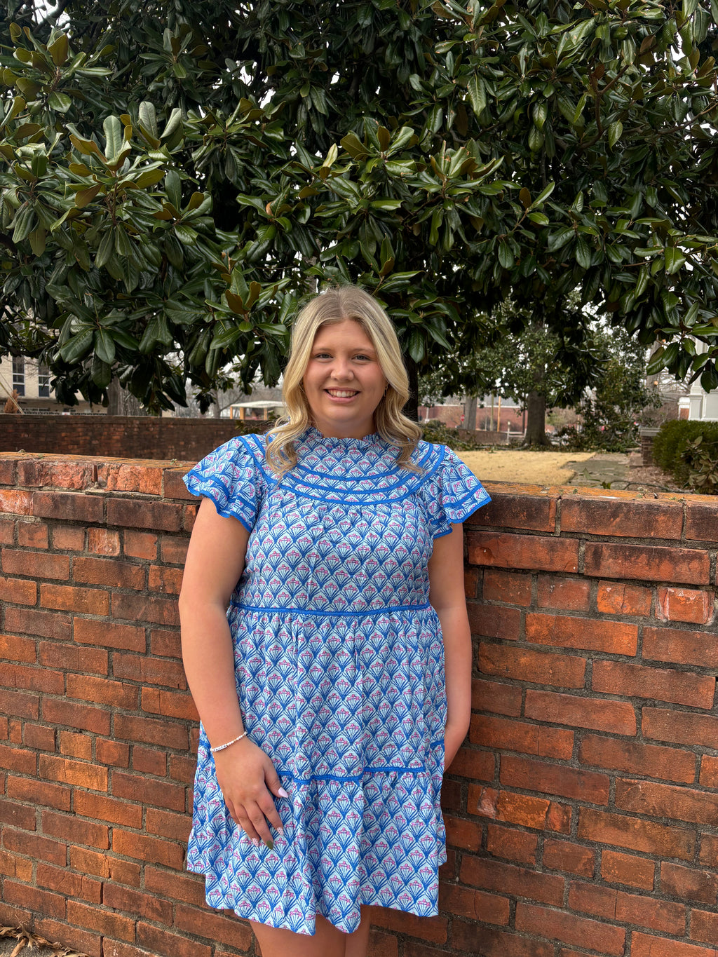 Woman in a blue dress standing infront of a brick wall with greenery in the background