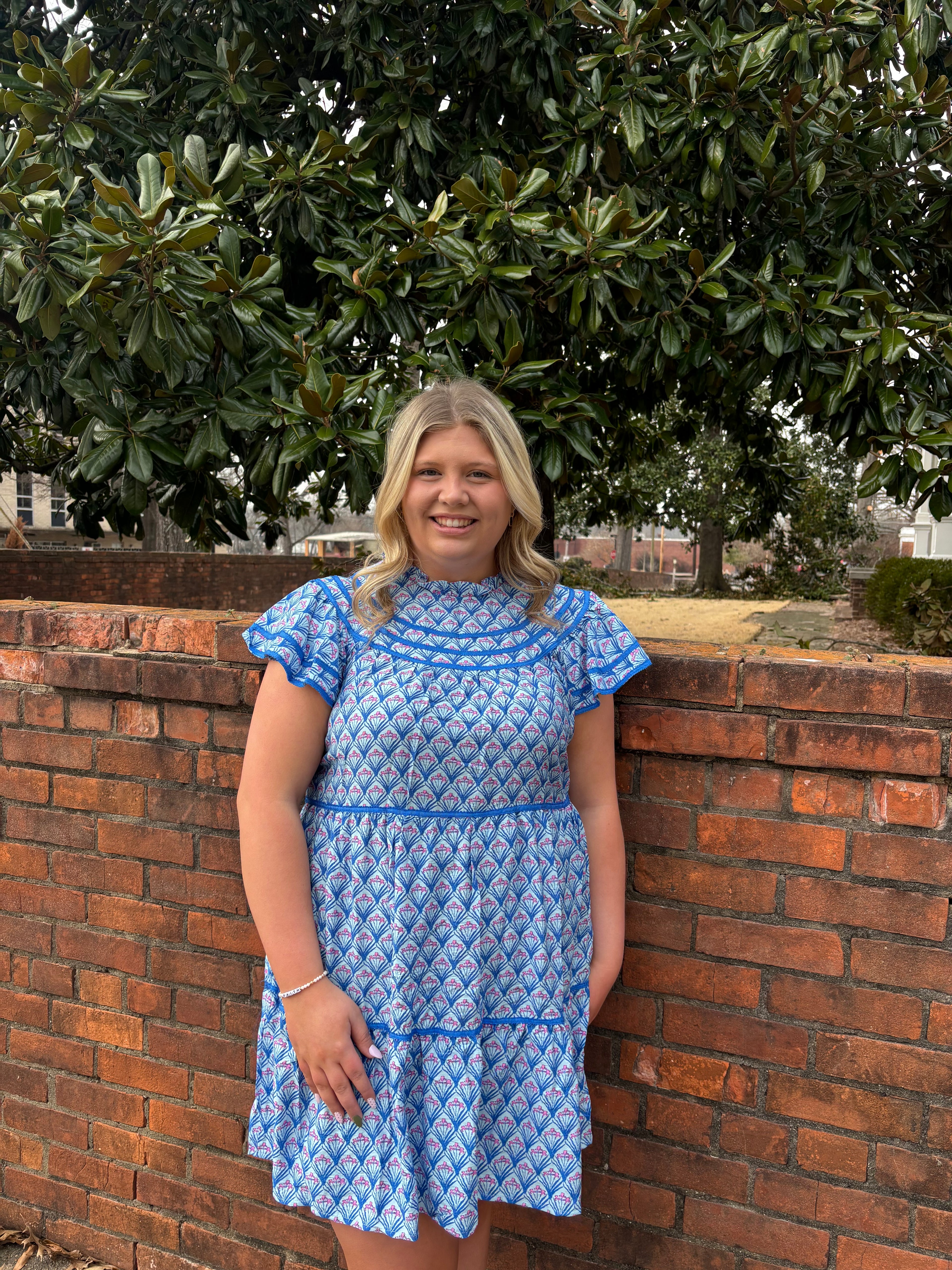 Woman in a blue dress standing infront of a brick wall with greenery in the background