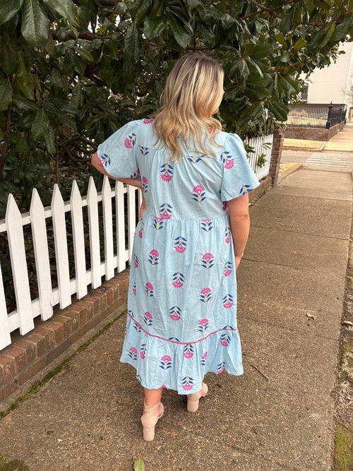 Person wearing a light blue dress with pink floral patterns on a sidewalk.