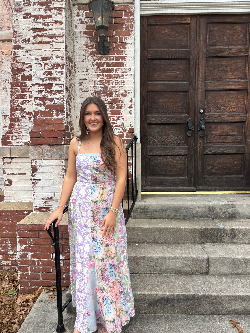 Woman in a floral dress standing in front of a wooden door.