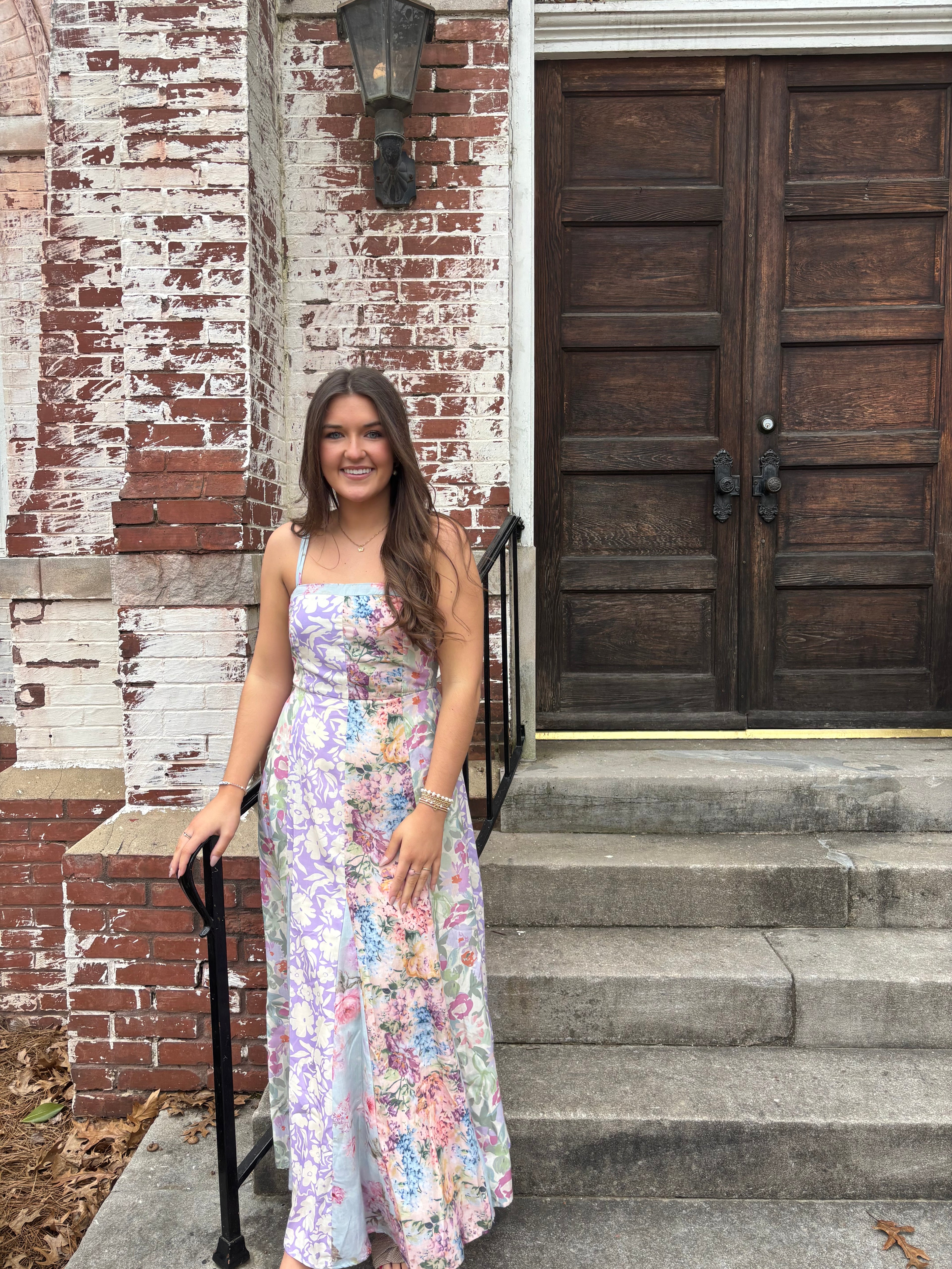 Woman in a floral dress standing in front of a wooden door.