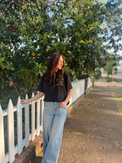 Woman standing on a sidewalk next to a white picket fence with trees in the background