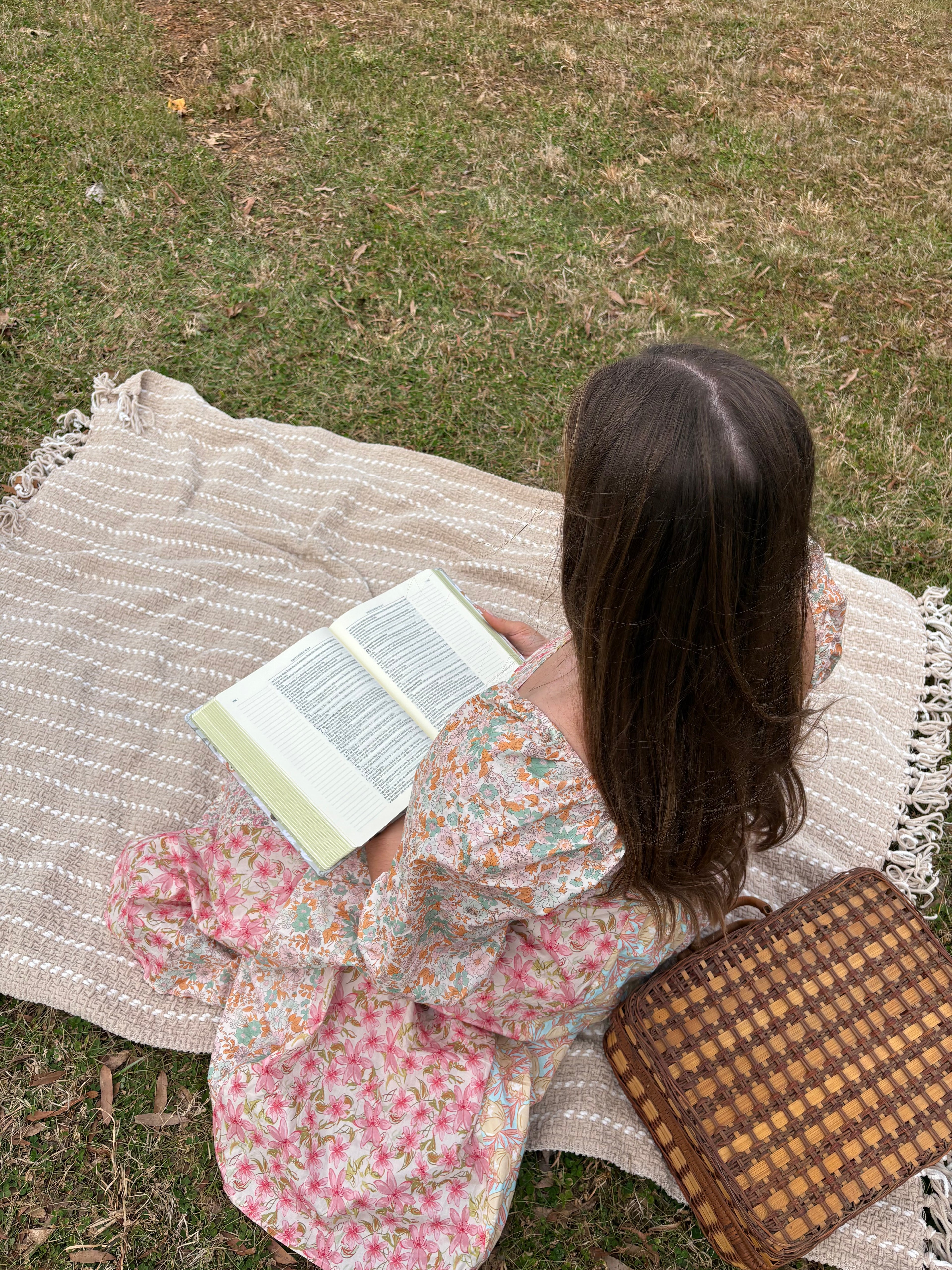 Person in a floral dress lying on a blanket with a bible outdoors