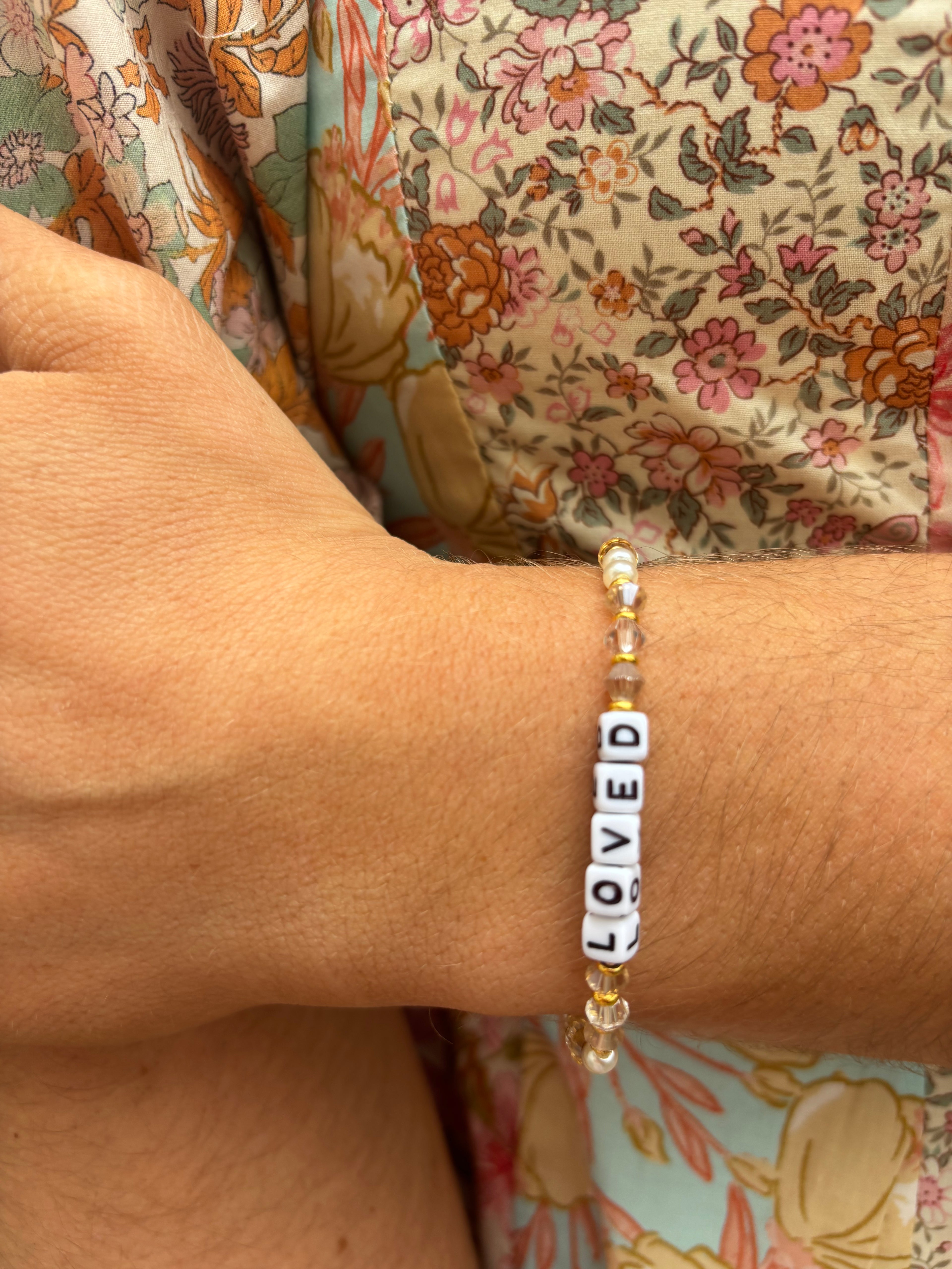 Bracelet with 'LOVED' beads on a wrist with floral fabric background
