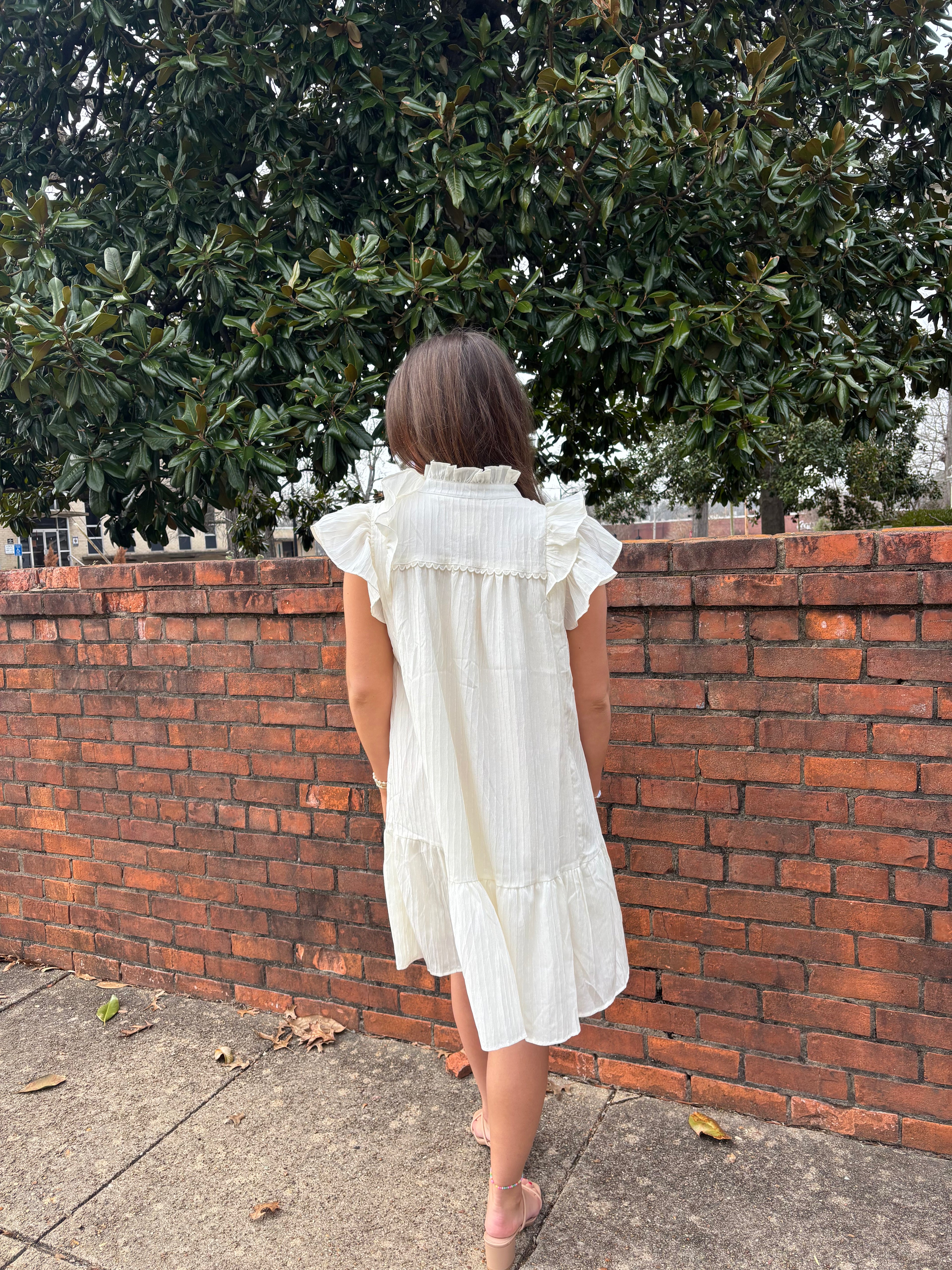 Woman in a white dress standing against a brick wall with greenery in the background