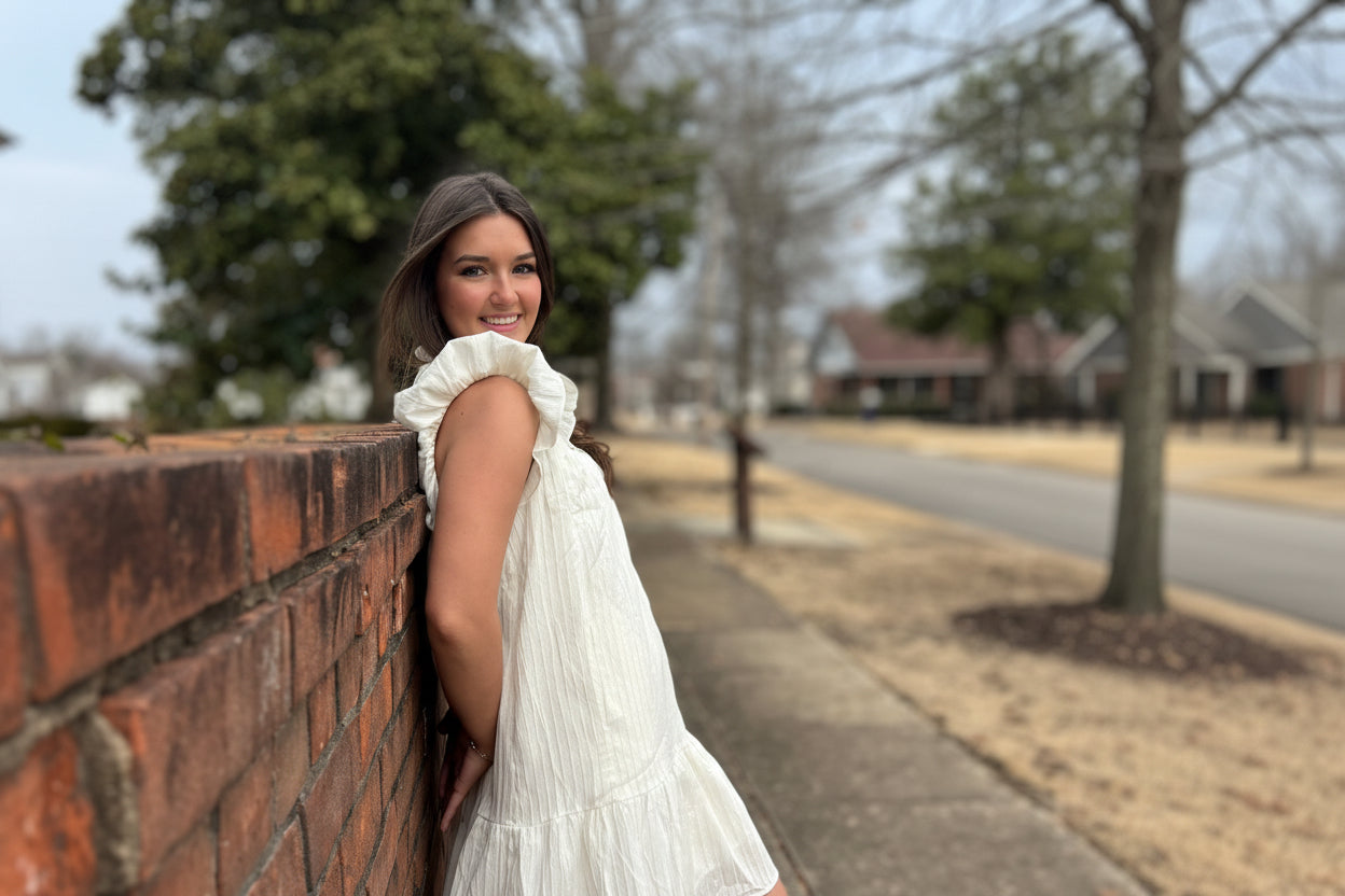 Woman in a white dress sitting on a brick wall outdoors