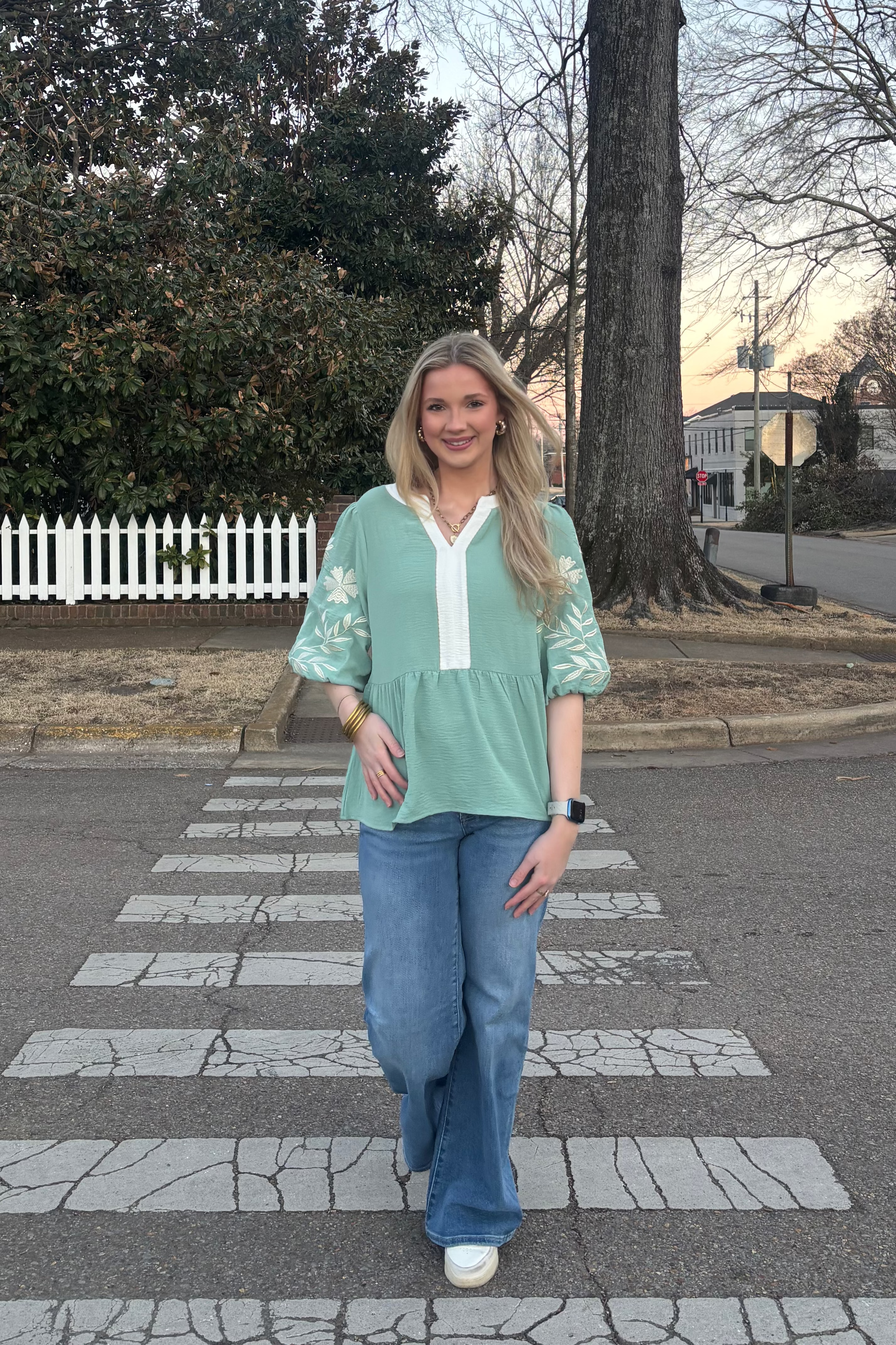 Woman wearing a green top with medium washed jeans standing outdoors
