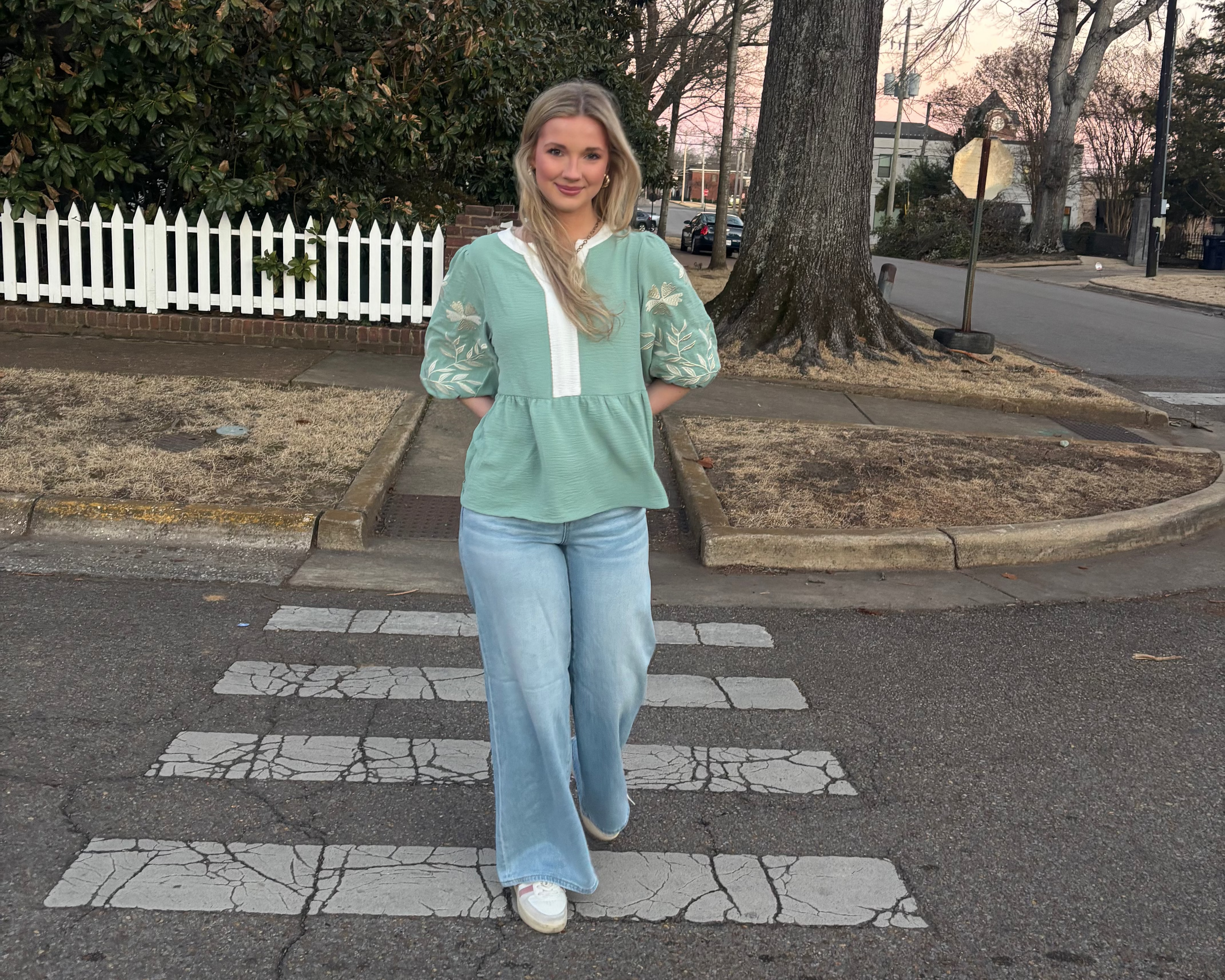 Woman standing on a crosswalk in an urban setting with trees and buildings in the background.