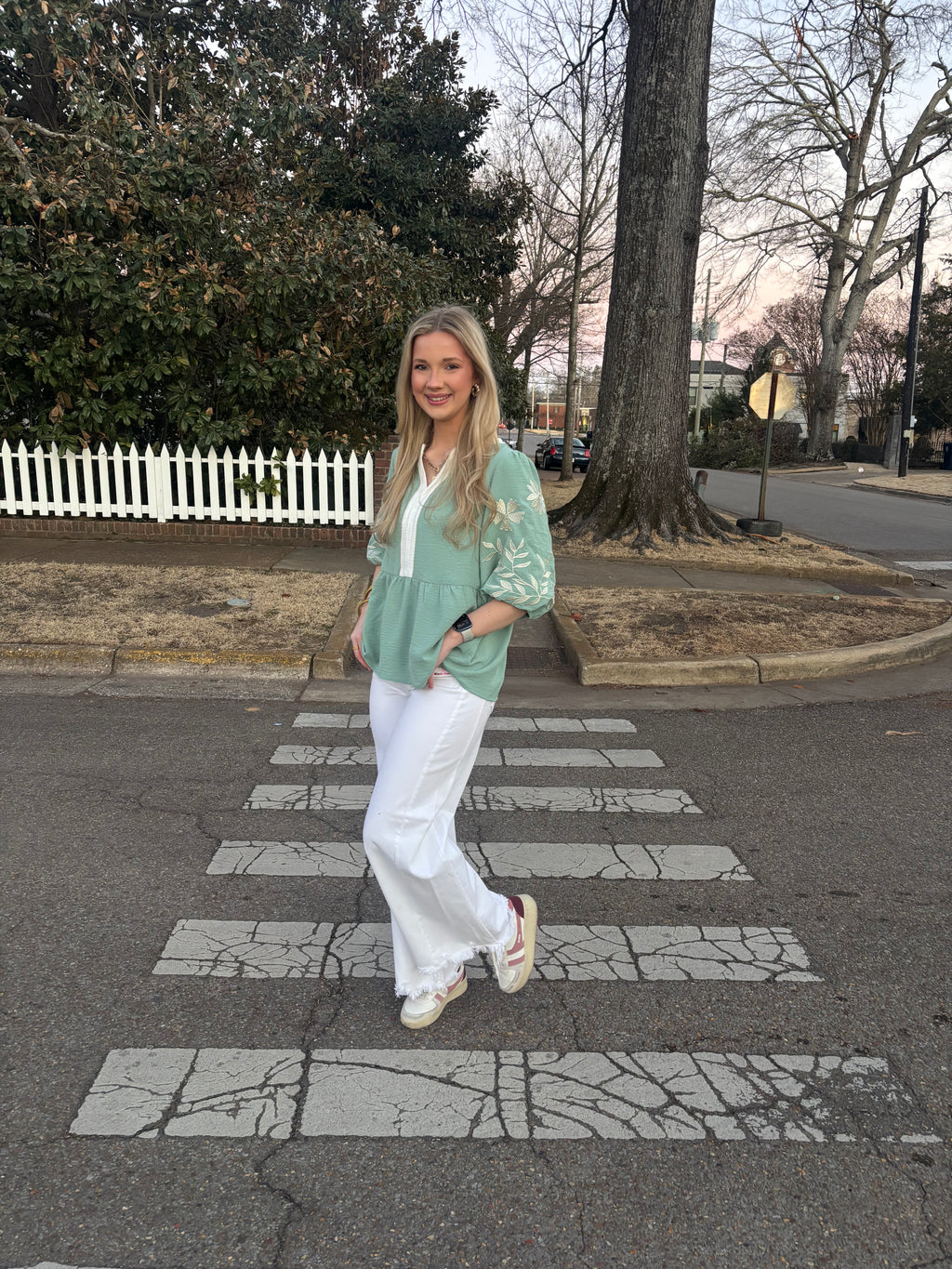 Woman wearing a green top with white jeans standing outside