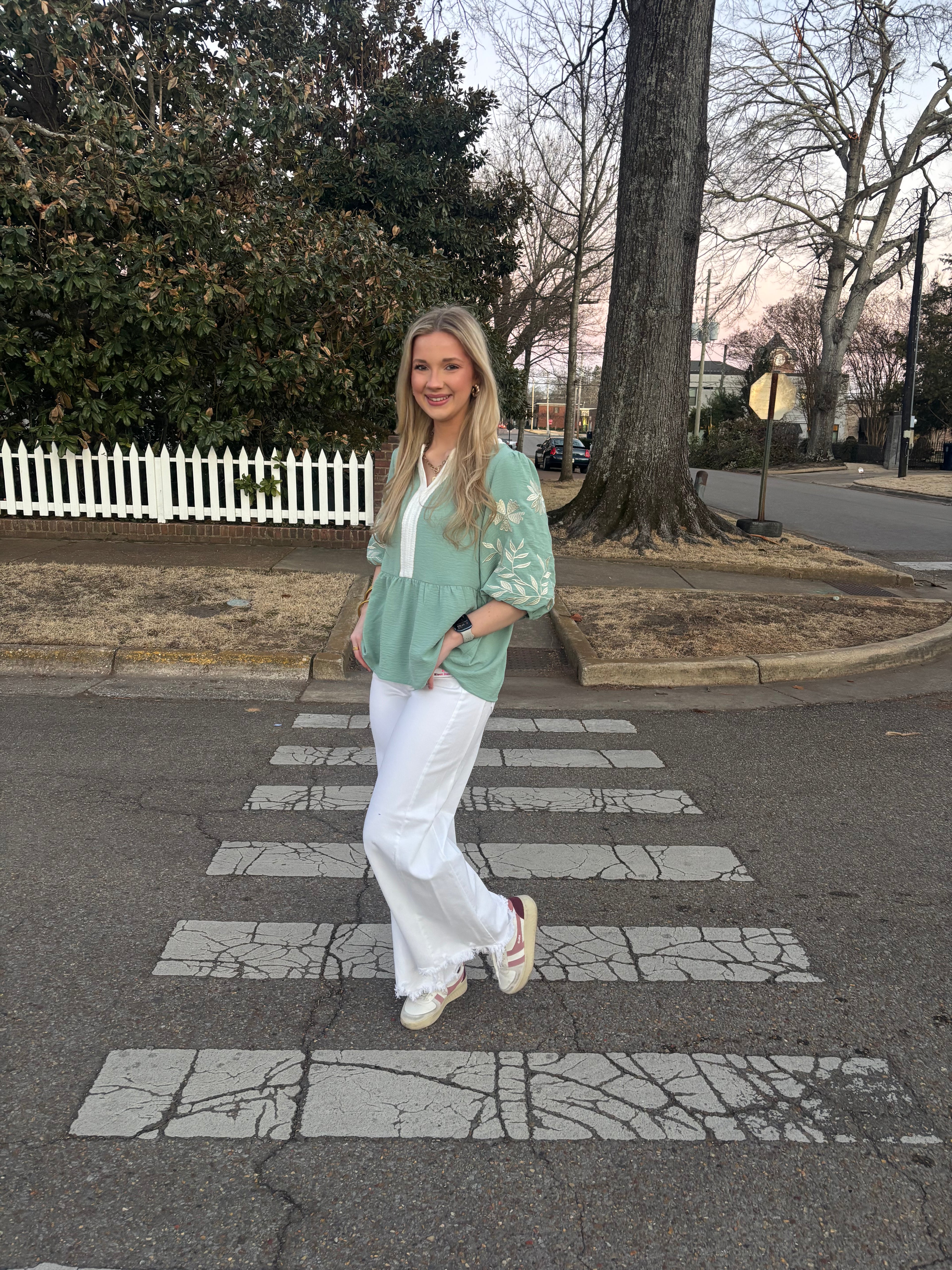 Woman wearing a green top with white jeans standing outside