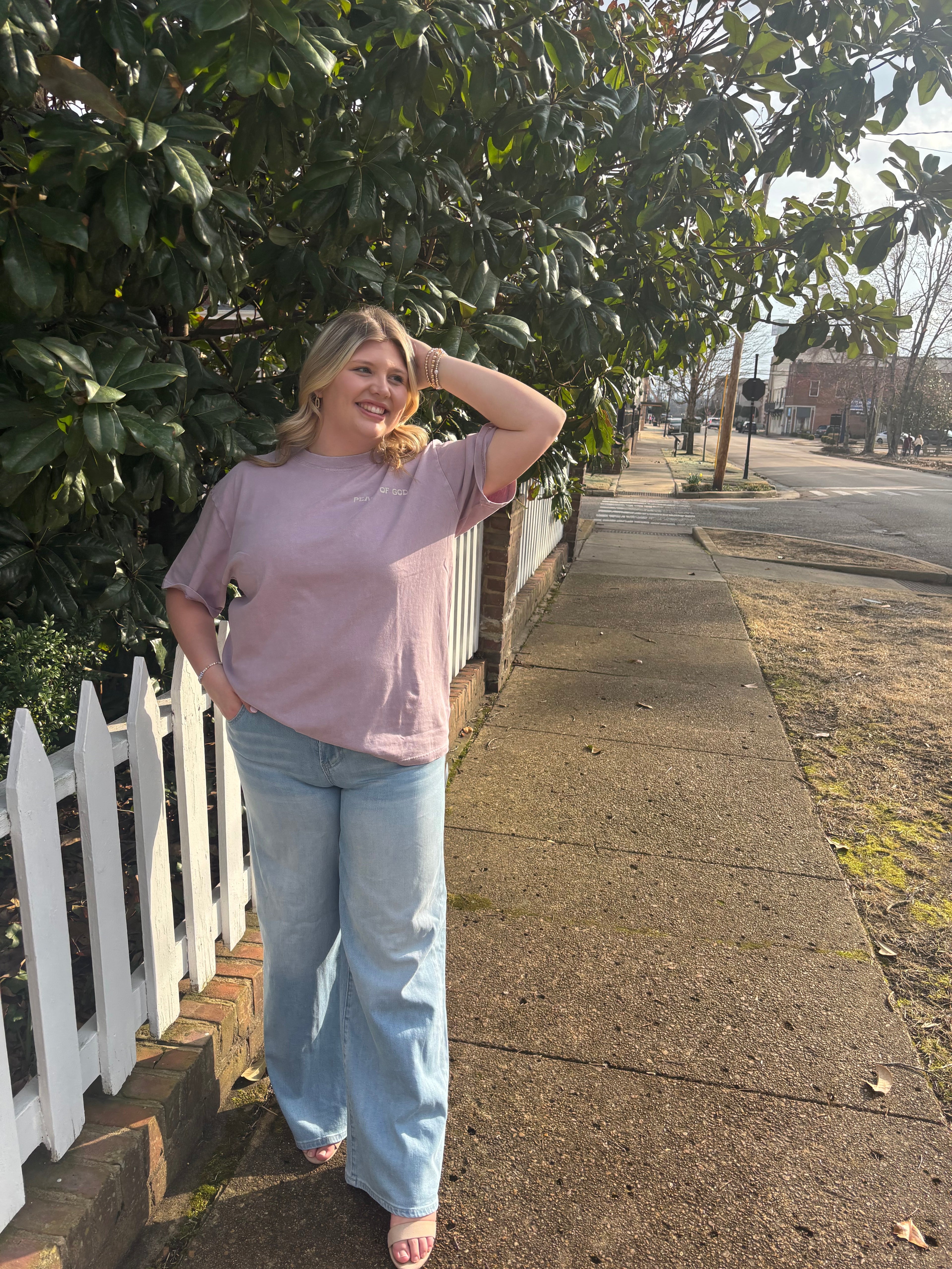 Person standing on a sidewalk next to a white picket fence with greenery around