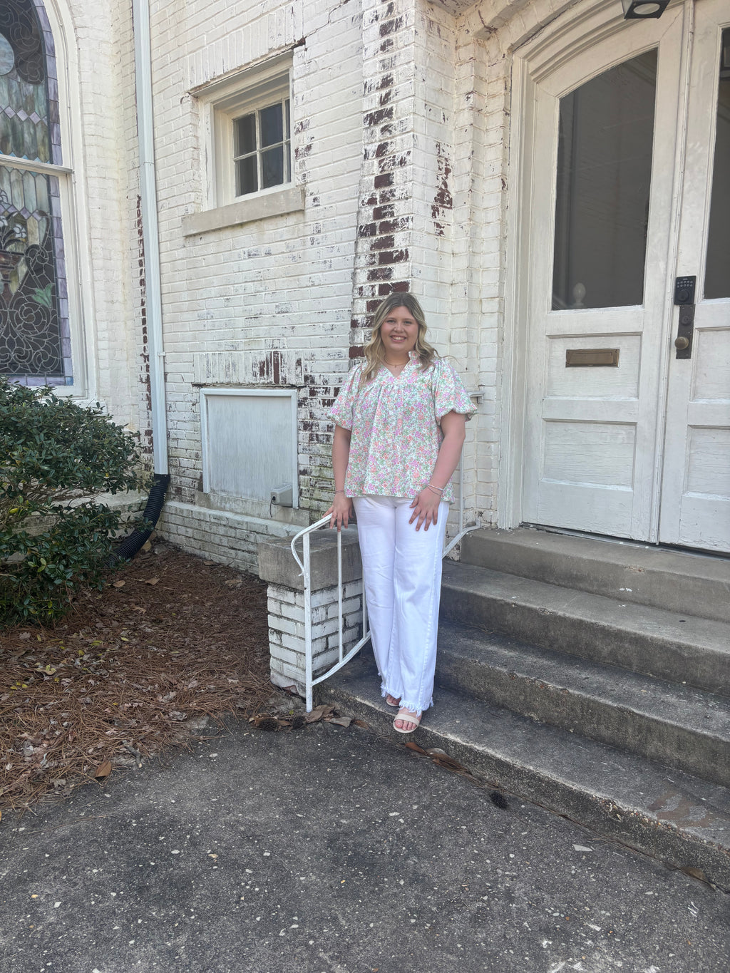 a woman wearing a floral blouse standing in front of a white brick church
