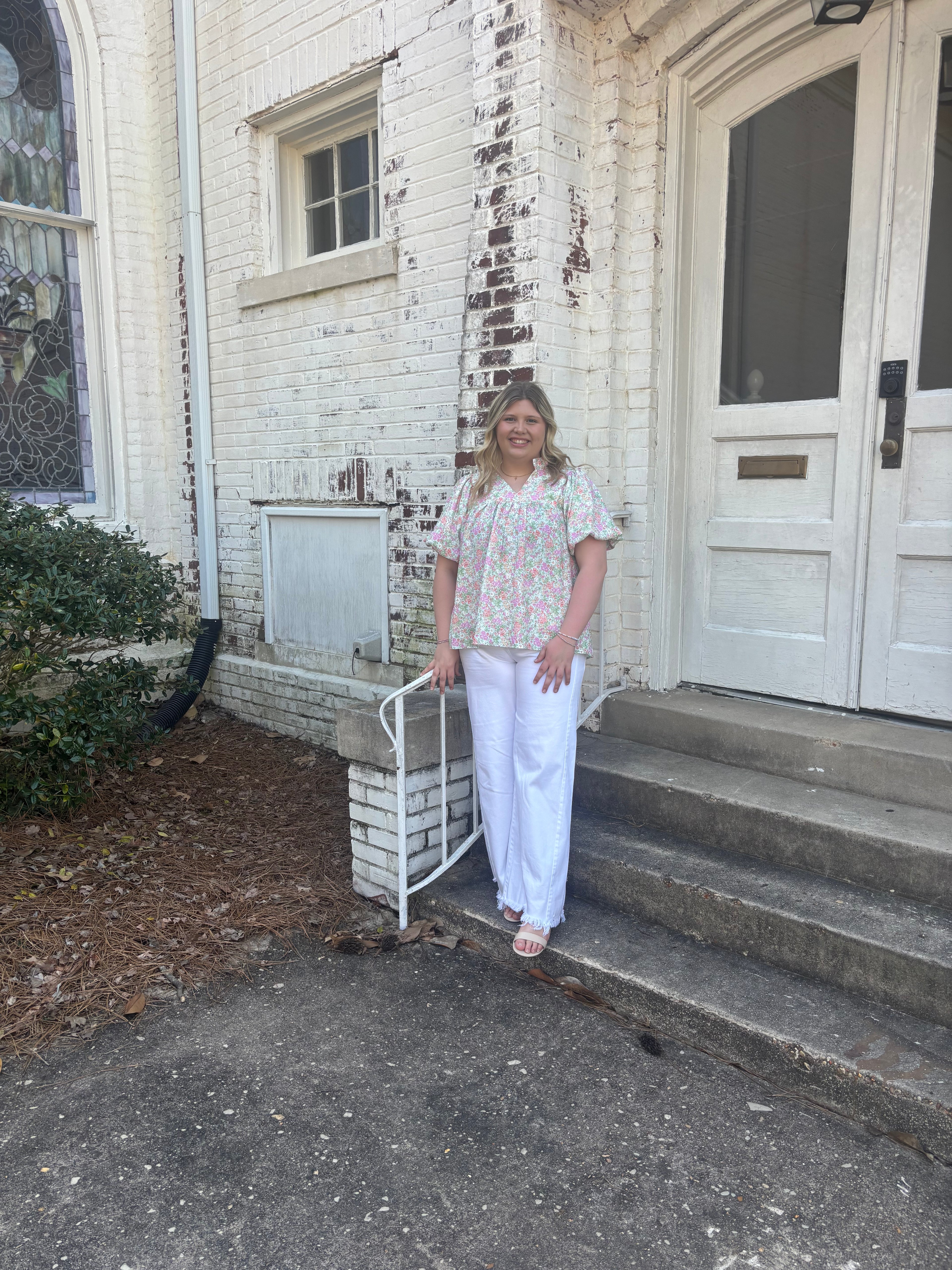 a woman wearing a floral blouse standing in front of a white brick church