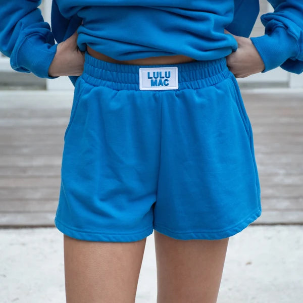 Person wearing blue shorts with a visible brand label, standing against a neutral background.