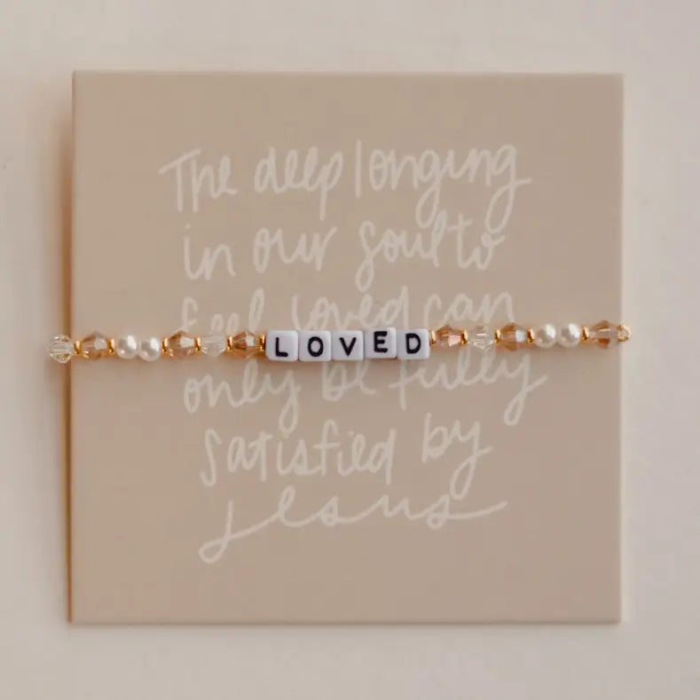 Bracelet with letter beads spelling 'LOVED' on a card with motivational quote