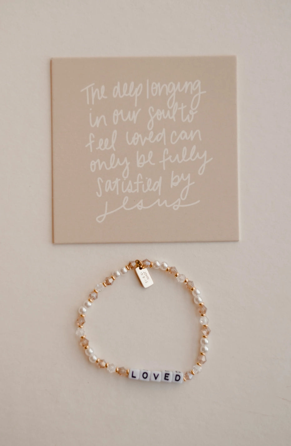 Bracelet with 'LOVED' beads on a beige background with motivational quote