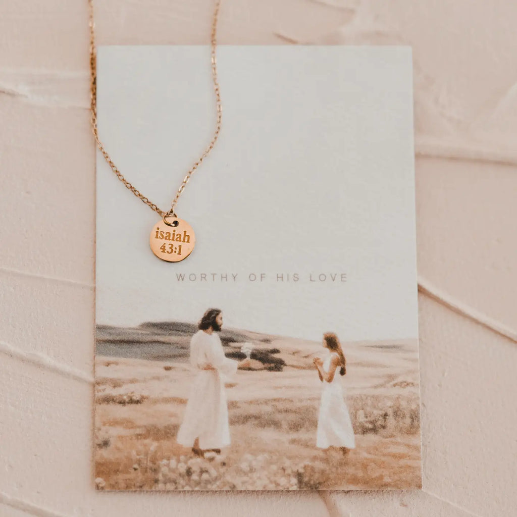 Gold necklace with a pendant on a card featuring an image of two people in white dresses.