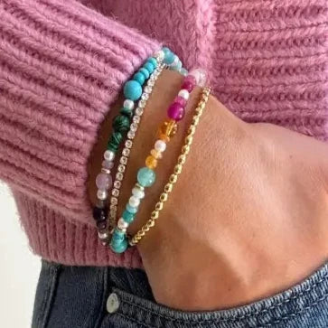Close-up of a hand wearing colorful beaded bracelets on a pink sweater background